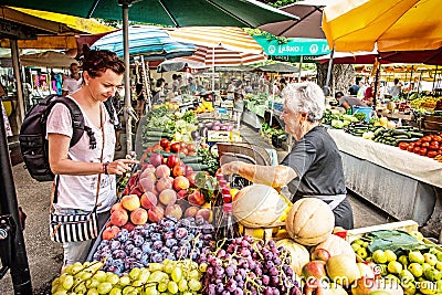 Young tourist woman buying fresh fruit from old woman at market Editorial Stock Photo